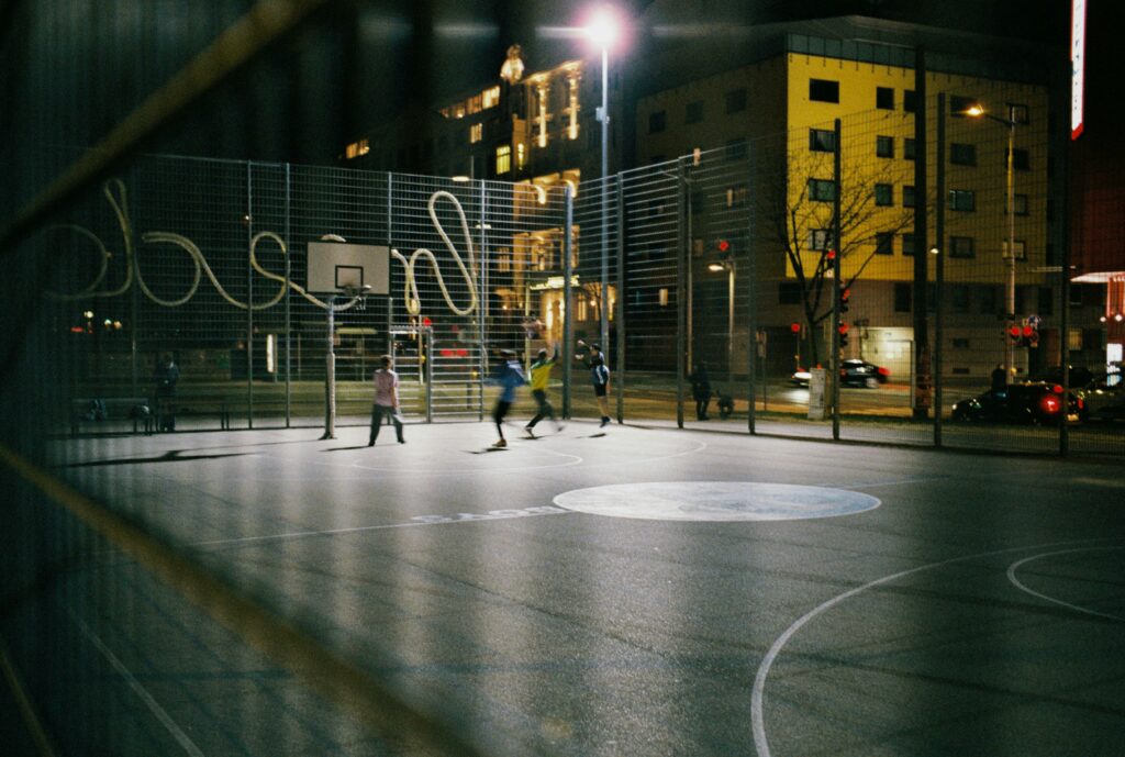 Men playing basketball on an urban court in Vienne at night.